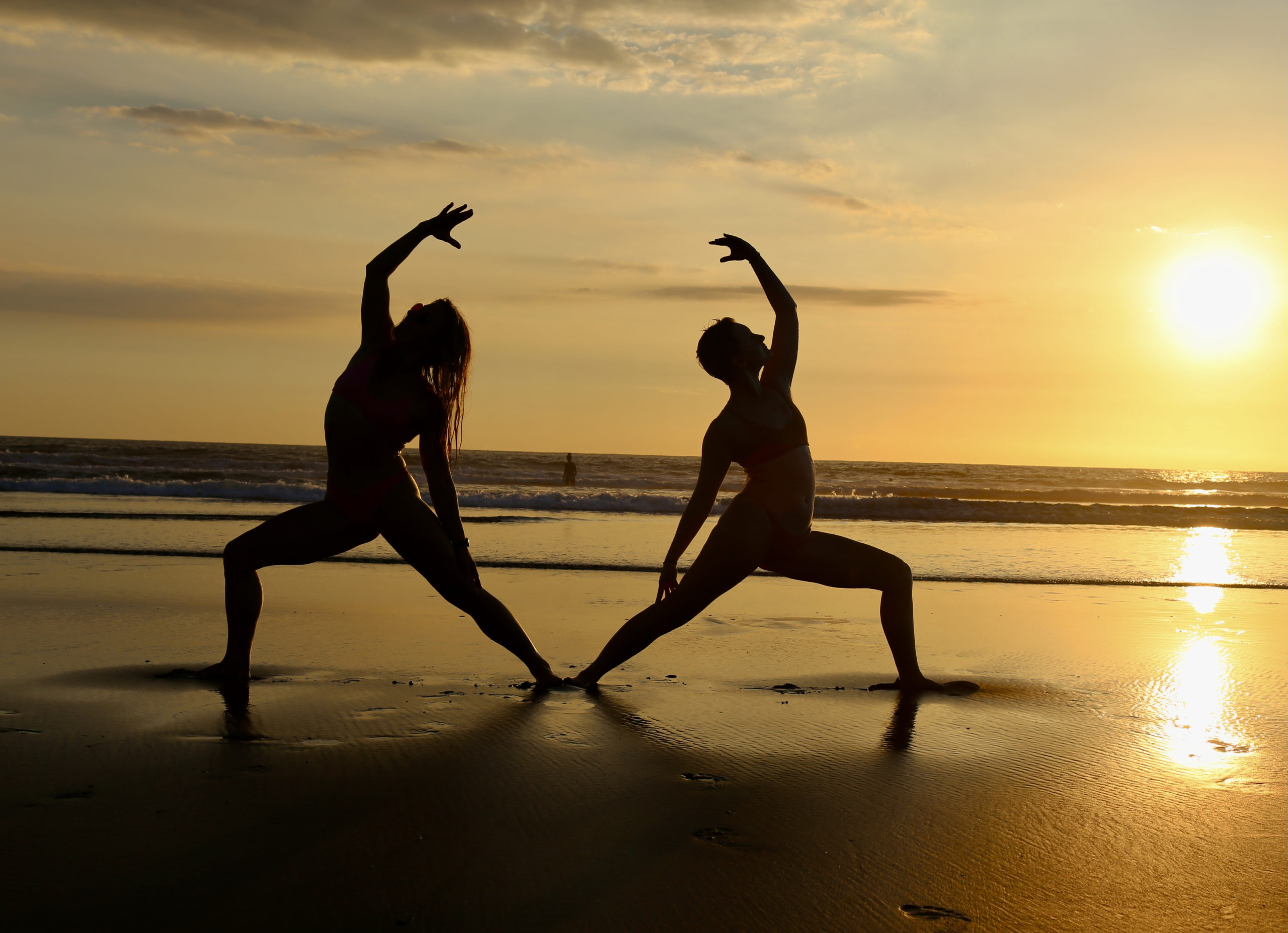 Silhouettes of two yogis at sunset on the beach in back to back reverse warrior pose