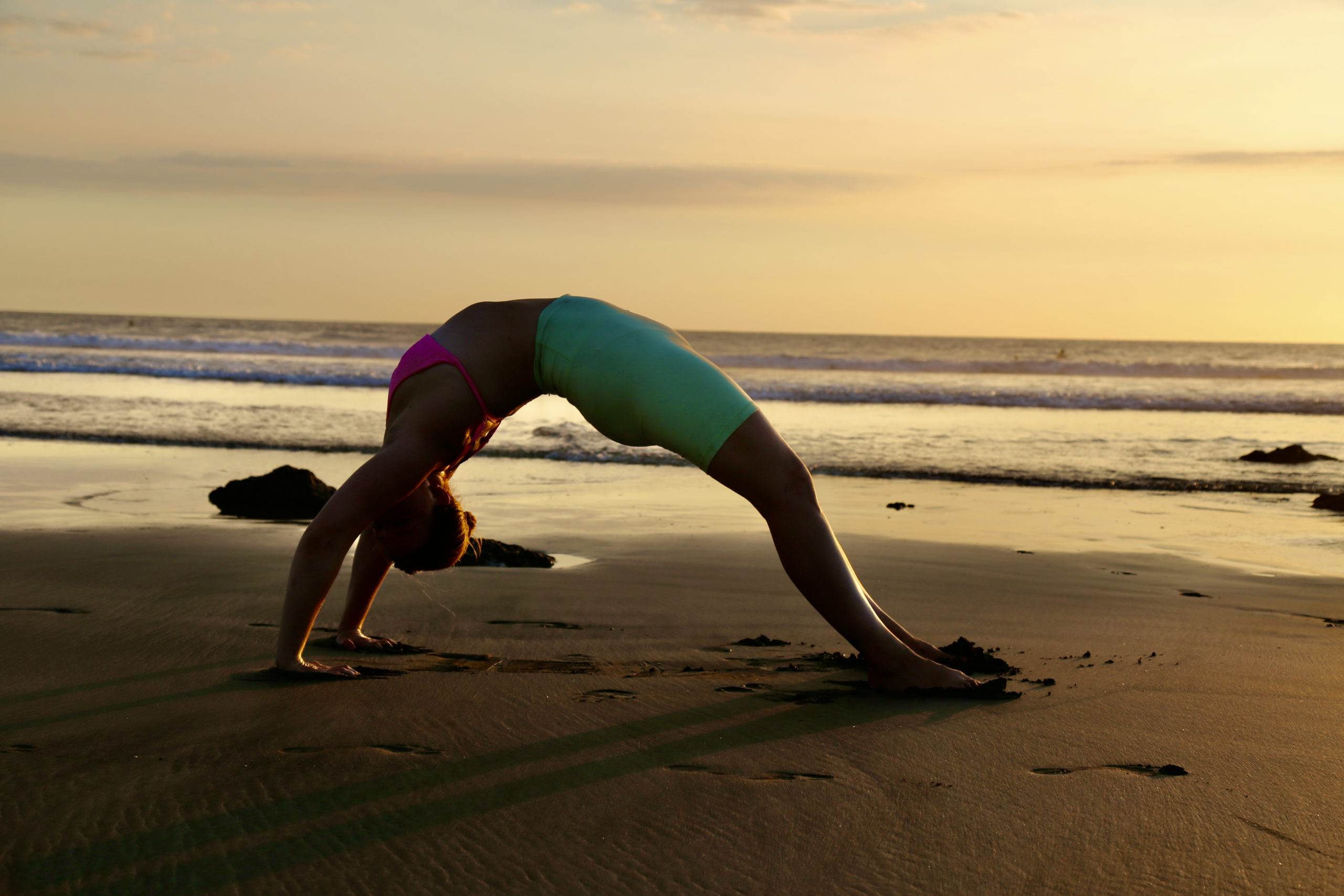 Yoga woman in wheel pose on the beach at sunset in costa rica