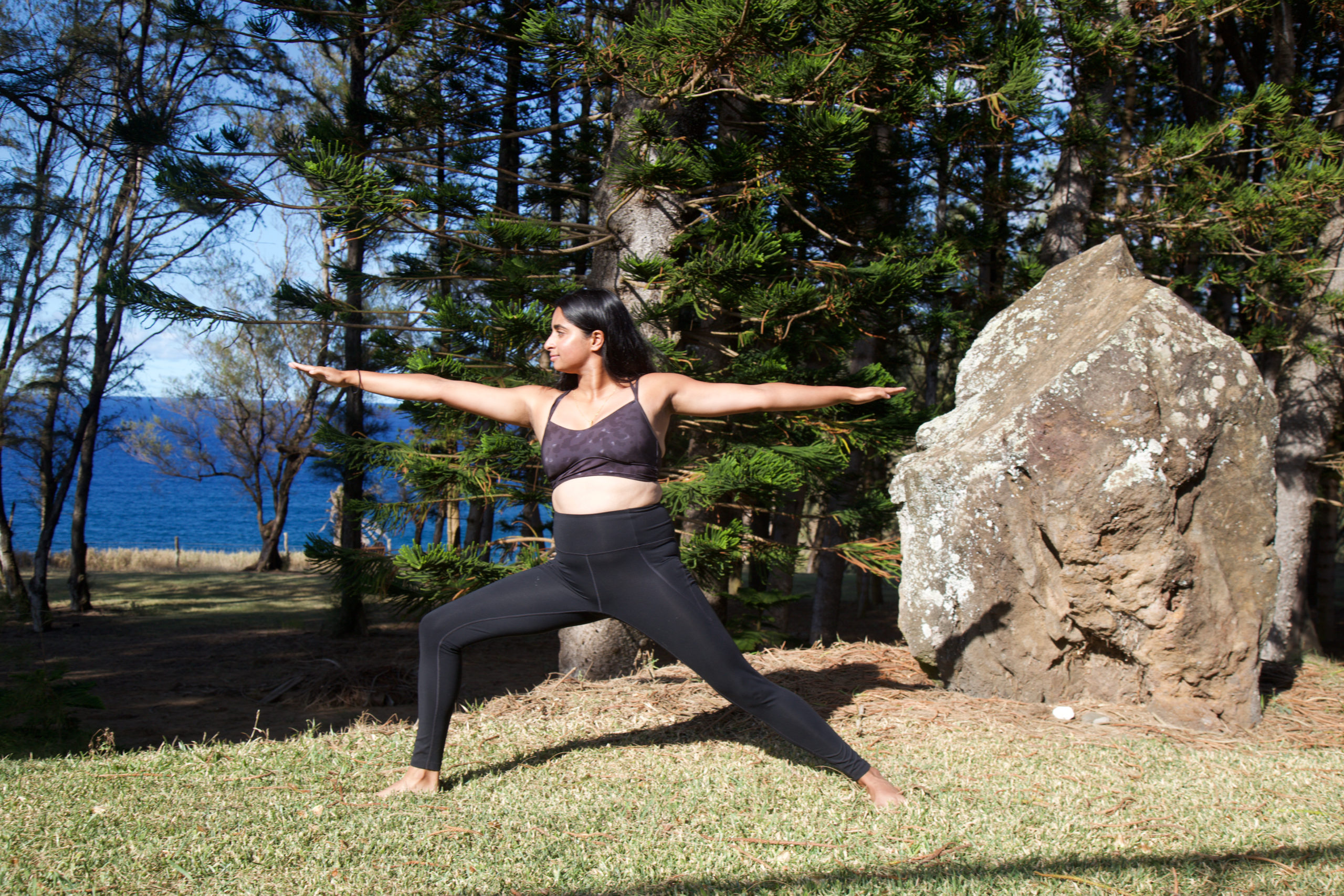 Yoga girl in all black outfit does warrior two pose by a boulder and forest