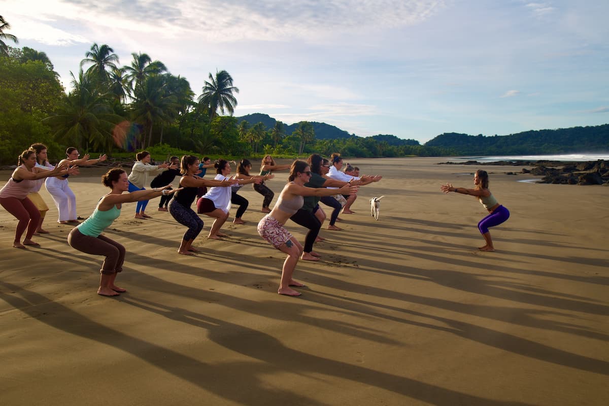 Students practicing Chair Pose on the beach during morning yoga teacher training in Costa Rica.